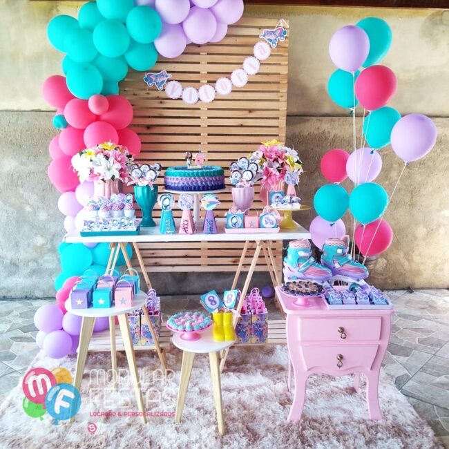 Decoração temática Patins Pegue e Monte decorado com mesa cavalete, par de mesinhas tripé, cômoda bombê rosa e painel de madeira ripado.
