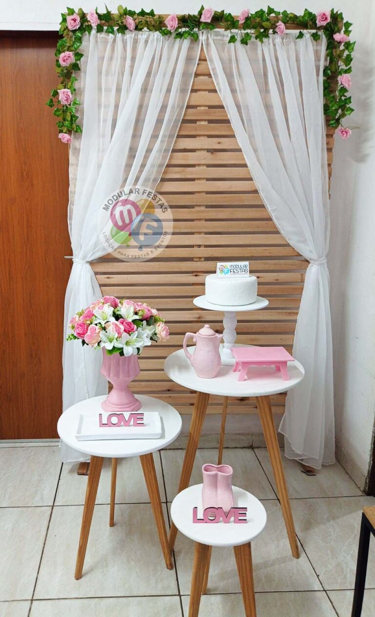 Kit Pegue e Monte adulto e juvenil festa temática Chá de Panelas branco e rosa. Composto por um trio de mesas tripé de madeira com tampo branco, painel ripado de pinus decorado com folhagens e buquê de flores permanentes e véu com caimento para as laterais além de vários outros itens decorativos.